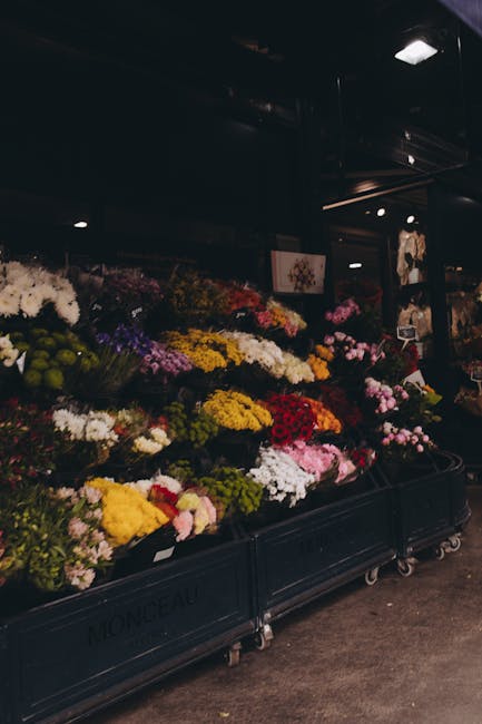 A display of freshly cut flowers arranged in black metal carts at a florist shop, featuring a variety of seasonal blooms in vibrant colours such as yellow, white, pink, red, purple, and green. The flo